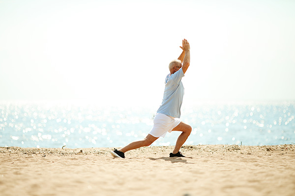 A person performs a yoga pose on a sandy beach with the ocean in the background.