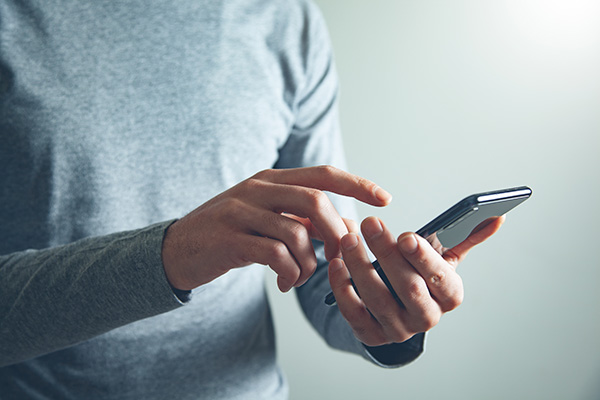 Person wearing a gray long-sleeve shirt using a smartphone.