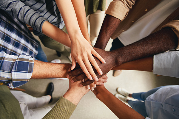 A diverse group of people standing in a circle with their hands stacked in the center, symbolizing unity and teamwork.