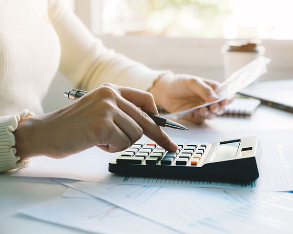 Person using a calculator while holding a piece of paper, surrounded by documents on a table.