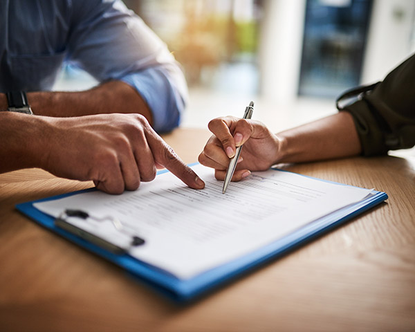 Two people reviewing and discussing a document on a clipboard, with one person pointing and the other holding a pen.