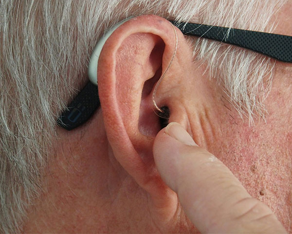 Close-up of a person inserting a hearing aid into their ear, with a finger pointing towards it.