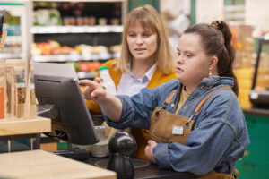 Portrait of young woman with Down syndrome learning to use cash register during occupational training in supermarket