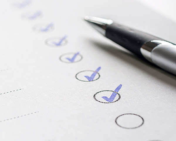 A checklist with several items ticked off in blue ink lies on a sheet of paper, with a pen resting on top.