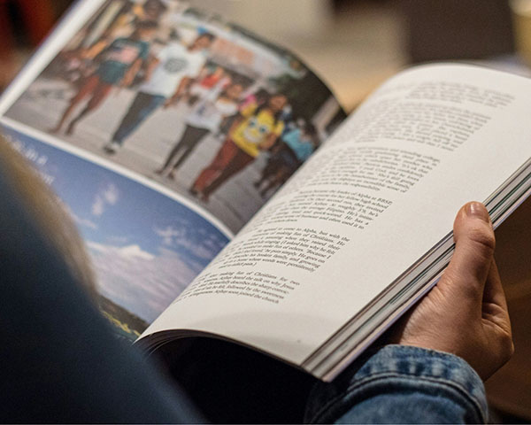 Person holding an open book with text on the right page and a blurred image of people walking on the left page.