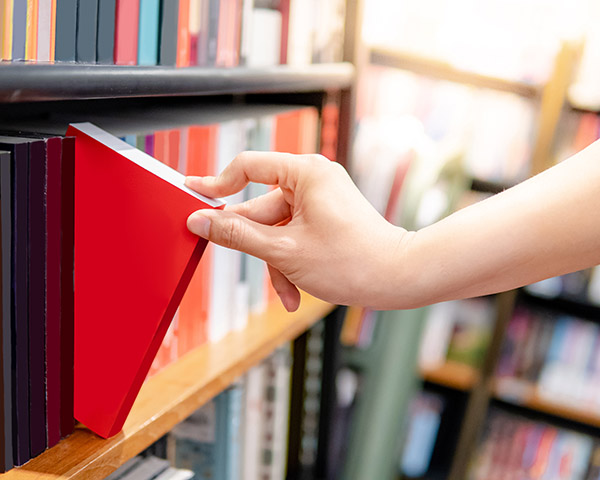 A hand pulls a red book from a shelf in a library.