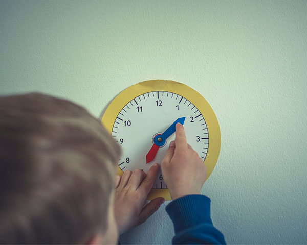 A child adjusts the hands of a toy clock on a wall.