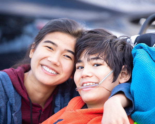 Two smiling individuals, one with an oxygen tube, are close together.