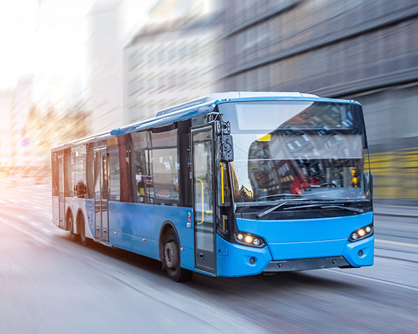 A blue city bus travels through an urban street with blurred surroundings, indicating motion.