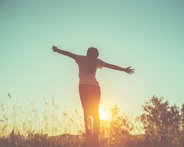 Silhouette of a person standing in a field with arms outstretched towards the sky during sunset.