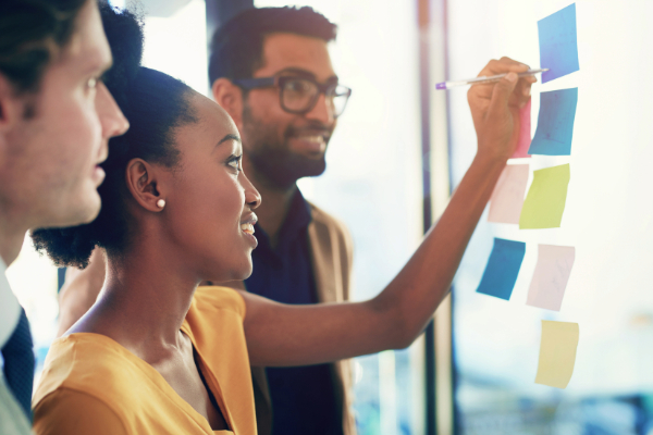 Woman writing on a mood board with team members during a team business meeting